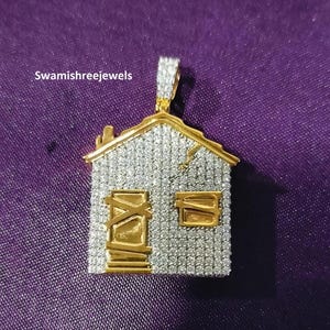 Può includere: Un ciondolo a forma di casa con tetto e porta dorati, incrostato di piccole pietre scintillanti. Il ciondolo ha un'attaccatura dorata ed è posto su uno sfondo viola. Il testo "Swamishreejewels" è visibile.