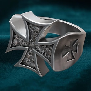 Peut inclure: Bague argentée ornée d'une croix de fer ornée de petits crânes. La bague présente une finition en métal brossé. Le design gothique est détaillé, avec la croix comme élément central.