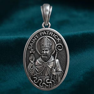 May include: Silver Saint Patrick pendant with an oval shape. The pendant features an engraved image of Saint Patrick holding a shamrock and staff, with the words "SAINT PATRICK" around the edge.
