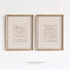 May include: Two framed prints with gold-colored frames. Each print features a beige and white checkered background with a central, textured, beige rectangle containing script. The prints are hung on a white wall.