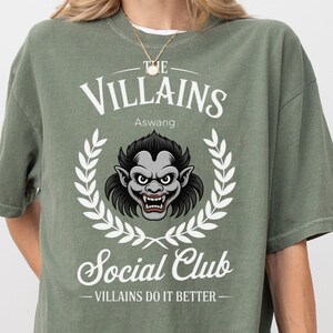 May include: Moss green t-shirt with the text "THE VILLAINS Social Club" and a graphic of a monster inside a laurel wreath. The shirt also has the text "VILLAINS DO IT BETTER".