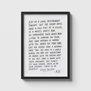 May include: A black framed wall art print featuring white background with black handwritten text that reads: EAT AT A LOCAL RESTAURANT TONIGHT. GET THE CREAM SAUCE. HAVE A COLD PINT AT 4 O'CLOCK IN A MOSTLY EMPTY BAR. GO SOMEWHERE YOU'VE NEVER BEEN. -A.B.
