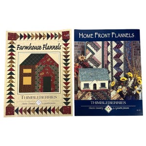 May include: Two quilting pattern books titled "Farmhouse Flannels" and "Home Front Flannels" by Thimbleberries. The "Farmhouse Flannels" book features a house design, while the "Home Front Flannels" book showcases quilt patterns.