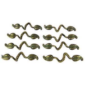 May include: Eight brass leaf-shaped drawer pulls. Each pull features a wavy stem with two leaves. The leaves have a green hue, and the brass has a polished finish. These decorative pulls are ideal for furniture restoration.