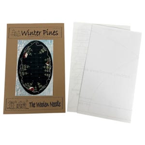 May include: A craft kit featuring a winter scene with pine trees and a house, titled "Winter Pines" and "The Woolen Needle." The kit includes a brown card with the design and white paper sheets.