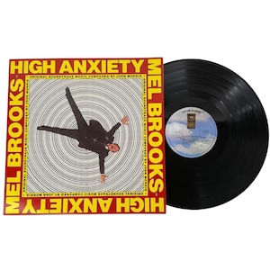 May include: A vinyl record album for the movie "High Anxiety" by Mel Brooks. The album cover is red and yellow with a black and white image of a man falling. The album is next to the vinyl record.