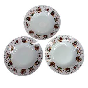 May include: Three white ceramic bowls with a festive Christmas design. The rims are decorated with red hearts, Santa Claus figures, and Christmas trees. The bowls are round and have a shallow depth, suitable for serving soups or desserts.