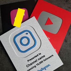 May include: A selection of social media recognition awards. The awards display the logos of Instagram, YouTube, and another platform. The Instagram award is light grey with a blue logo and text. The YouTube award is red with a grey play button.