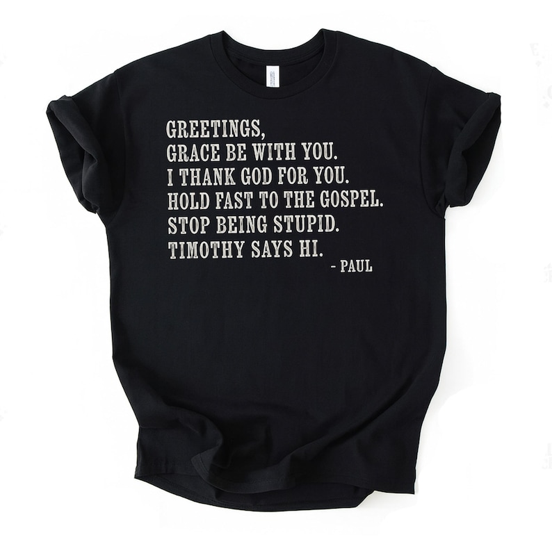 Black t-shirt with white text reading "Greetings, grace be with you. I thank God for you. Hold fast to the gospel. Stop being stupid. Timothy says hi. - Paul."