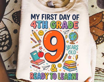 Puede incluir: Una sudadera de cuello redondo color crema con un estampado gráfico colorido que dice MY FIRST DAY OF 4TH GRADE, 9 YEARS OLD y READY TO LEARN. El diseño incluye ilustraciones de un número nueve grande de color naranja, libros, lápices, un globo terráqueo y una manzana.