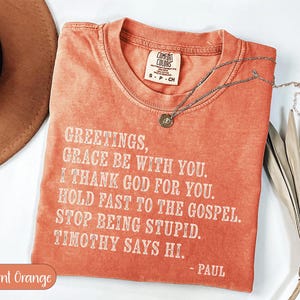 Burnt orange t-shirt with "Greetings, grace be with you. I thank God for you. Hold fast to the gospel. Stop being stupid. Timothy says hi. - Paul" text.