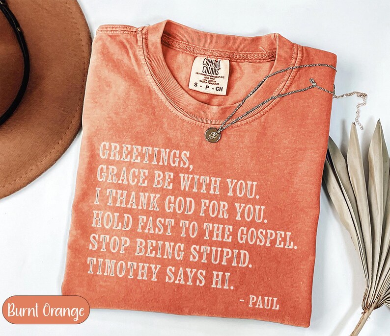 Burnt orange t-shirt with "Greetings, grace be with you. I thank God for you. Hold fast to the gospel. Stop being stupid. Timothy says hi. - Paul" text.