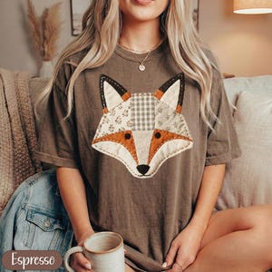 May include: Espresso-colored t-shirt featuring a patchwork fox design. The fox has orange, white floral, and gray checkered fabric details. The shirt is a relaxed fit and has short sleeves. The word "Espresso" is printed on the bottom left.