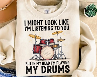 May include: Cream-colored sweatshirt with the text "I MIGHT LOOK LIKE I'M LISTENING TO YOU BUT IN MY HEAD I'M PLAYING MY DRUMS." The graphic features a drum set in red, gold, and black.
