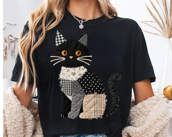 Puede incluir: Una camiseta negra de manga corta con un gran gráfico central de un gato construido con varios parches de tela acolchada. El diseño del gato incluye patrones de cuadros vichy en blanco y negro, lunares y beige sólido con ojos de color naranja brillante.