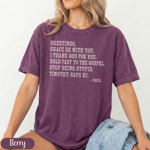 Purple t-shirt with "Greetings, Grace be with you. I thank God for you. Hold fast to the Gospel. Stop being stupid. Timothy says hi. - Paul" and "Berry" graphic.