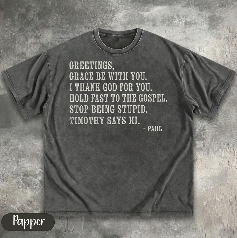 Dark grey t-shirt with "Greetings, grace be with you. I thank God for you. Hold fast to the gospel. Stop being stupid. Timothy says hi. - Paul" in white text.