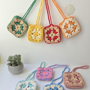 May include: A collection of seven small square crochet pouches, each featuring a central floral motif in various color combinations including green, yellow, red, orange, light blue, pink, and lavender, all with matching long crocheted straps.