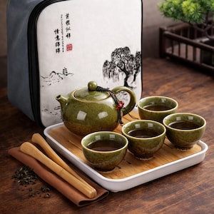Könnte beinhalten: Ein grünes Keramik-Teeservice mit Teekanne, vier Tassen und Bambusutensilien auf einem Holztablett. Das Set enthält eine Tragetasche mit einer Baumillustration und chinesischen Schriftzeichen.