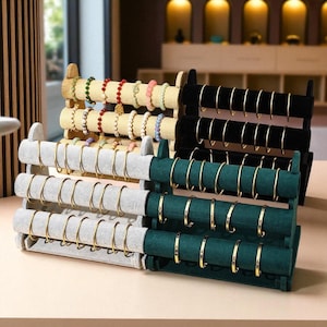 May include: A multi-tiered jewellery display stand showcasing bracelets. The stands are covered in black, green, and grey velvet, with wooden and black accents. Gold bracelets and beaded bracelets are displayed on the stands.