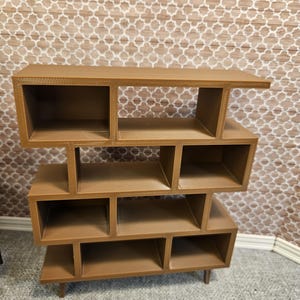 May include: A brown, mid-century modern style bookshelf with multiple cubby shelves. The bookshelf is made of a solid material and has a tiered design. The shelves are various sizes and shapes, and the unit stands on four short legs.