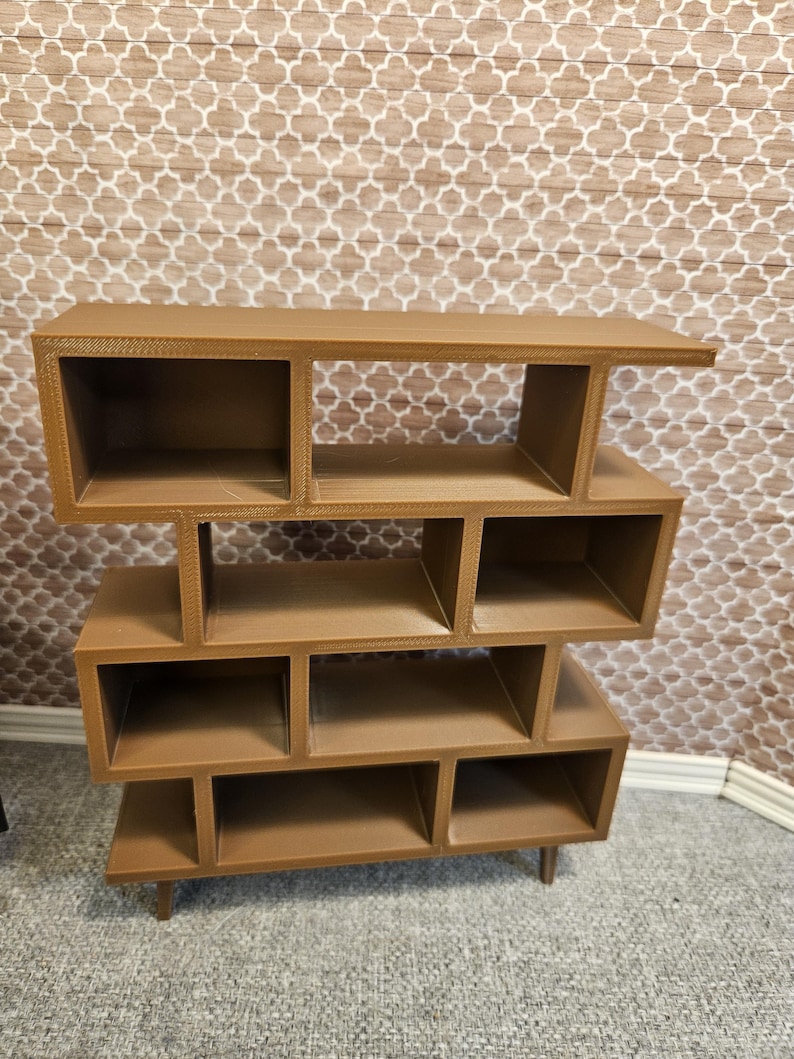 May include: A brown, mid-century modern style bookshelf with multiple cubby shelves. The bookshelf is made of a solid material and has a tiered design. The shelves are various sizes and shapes, and the unit stands on four short legs.