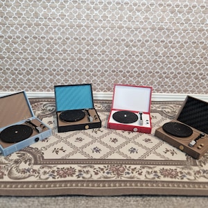 May include: Four miniature record players in various colors: light blue, black, red, and brown. Each player has a black record, a tone arm, and a speaker. The players are displayed on a patterned rug.