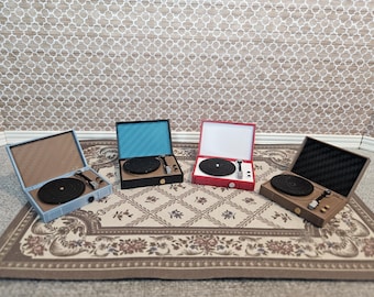 May include: Four miniature record players in various colors: light blue, black, red, and brown. Each player has a black record, a tone arm, and a speaker. The players are displayed on a patterned rug.