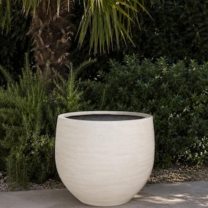 Op de afbeelding: Een grote, bolvormige plantenbak met een gladde, gebroken witte, matte afwerking. De container heeft een brede, ronde opening aan de bovenkant met een donkere binnenkant en een bolvormig lichaam dat naar de onderkant toe iets smaller wordt.