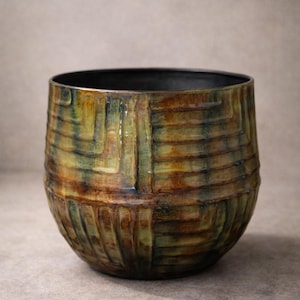 Könnte beinhalten: Handgefertigte Keramikschale mit einem strukturierten, gewebten Muster. Die Schale hat eine Farbpalette aus Grün-, Braun- und Gelbtönen mit einem dunklen Innenraum. Die runde Form und das einzigartige Design machen sie zu einem dekorativen Stück.