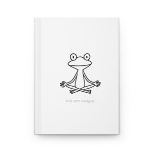 Peut inclure: Un journal blanc avec un dessin au trait noir d'une grenouille en position de yoga. Le texte "THE ZEN FROGUS" est en dessous de l'illustration de la grenouille. Le journal a un design minimaliste.