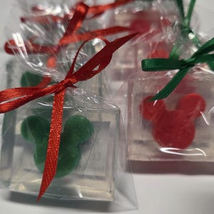May include: Several clear, square-shaped soaps individually wrapped in transparent plastic bags. Each soap contains a solid, opaque mouse-shaped figure in either red or green. The bags are tied with thin red or green satin ribbons at the top.
