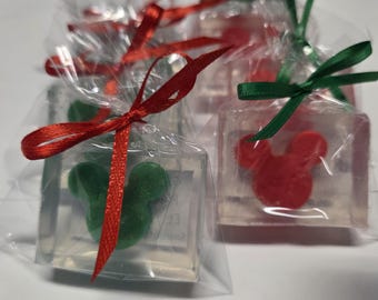 May include: Several clear, square-shaped soaps individually wrapped in transparent plastic bags. Each soap contains a solid, opaque mouse-shaped figure in either red or green. The bags are tied with thin red or green satin ribbons at the top.