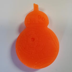 May include: Orange BB-8 droid-shaped item with detailed surface patterns. The item has a rounded body and a smaller, cylindrical head with a small antenna. The design is reminiscent of the Star Wars character.