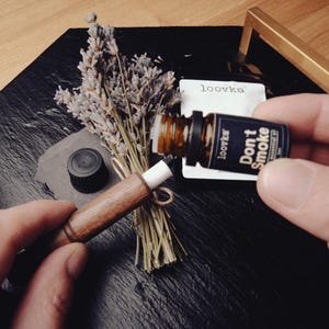 Puede incluir: Una composición con una pequeña botella marrón de aceite esencial con la etiqueta "Don't Smoke" y un difusor de aromaterapia de madera. También hay un ramo de lavanda seca y una pequeña tarjeta blanca con la marca "loovka".