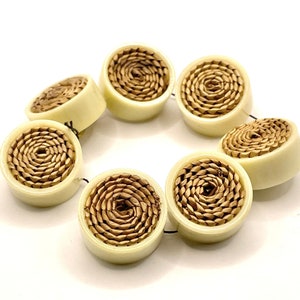 Può includere: Un set di sette bottoni rotondi color crema con un design a spirale intrecciato marrone al centro.