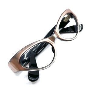 May include: A pair of cat-eye glasses with a rose gold frame and black arms. The lenses are clear.