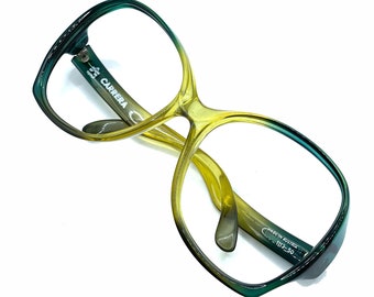 May include: Carrera eyeglasses featuring a gradient frame that transitions from dark teal to translucent yellow. The inner temple is printed with the text Carrera, Made in Austria, and 1113-50. These glasses have a large, rounded square shape.