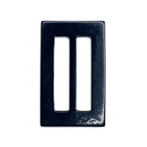 Op de afbeelding: Een rechthoekige, zwarte metalen gesp met twee verticale sleuven. De gesp heeft een glanzende afwerking en staat tegen een witte achtergrond. Dit hardware-onderdeel is waarschijnlijk voor tassen, riemen of andere accessoires.