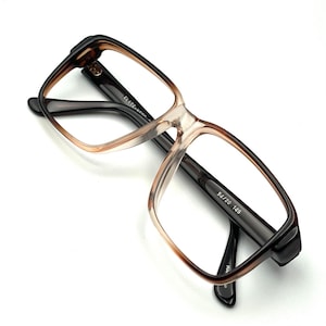 Puede incluir: Gafas rectangulares con montura marrón y beige degradado y patillas marrones oscuras. Las gafas tienen lentes transparentes y la talla es 54/20 145.