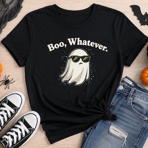 Puede incluir: Una camiseta negra de manga corta con el gráfico de un fantasma blanco que lleva gafas de sol negras. Sobre el fantasma, el texto "Boo, Whatever." aparece en letras blancas, rodeado de pequeños puntos blancos en el diseño.