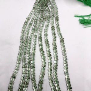 May include: A strand of faceted, translucent light green beads arranged in multiple vertical rows. The beads are strung on a thin green cord that terminates in a green tassel at the top. Each bead features a circular, multi-faceted surface.