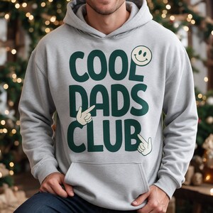 Świąteczny prezent dla taty: koszulka COOL DADS CLUB z uśmiechniętą buźką i dłońmi – zabawny pomysł dla ojców i mężczyzn rodzinnych