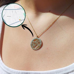 Puede incluir: Un collar de tono dorado con un colgante circular que presenta un diseño de mapa de calles recortado. El colgante cuelga de una delicada cadena dorada. Un gráfico circular insertado muestra un mapa detallado de Briarwood con calles.