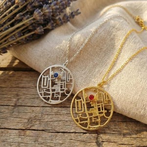 May include: Two pendant necklaces with intricate, openwork designs. One is silver-toned with a blue gemstone, the other gold-toned with a red gemstone. Both are on delicate chains, displayed on a wooden surface.