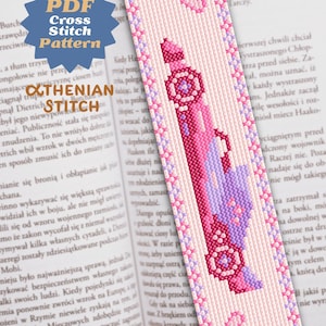 May include: A handmade cross-stitch bookmark with a pink and purple design. The bookmark features a detailed pattern of a stylized object, framed by a border of small flowers. The text "PDF Cross Stitch Pattern" is visible.