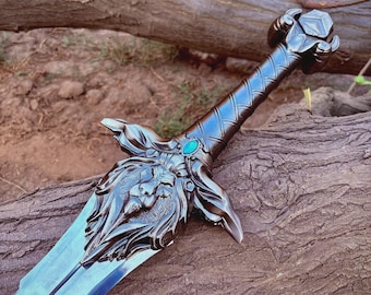 May include: A detailed, fantasy-style sword with a silver blade and a dark, ornate handle. The handle features a lion's head design and a turquoise gem. The sword is resting on a weathered log, suggesting an outdoor setting.