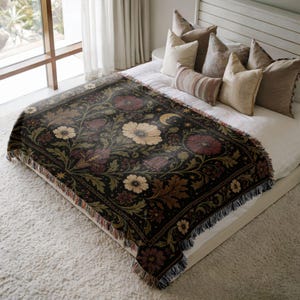 Peut inclure: Un plaid tissé présentant un fond sombre avec un motif botanique de fleurs, de feuilles et de vignes dans des tons crème, rouge et vert. Le design inclut des éléments célestes comme un croissant de lune et des étoiles, avec des franges.