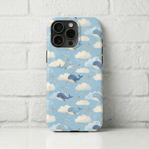 May include: A light blue phone case featuring a pattern of whales, clouds, and gold stars. The whales are blue and the clouds are white. The case has a glossy finish and a camera cutout.