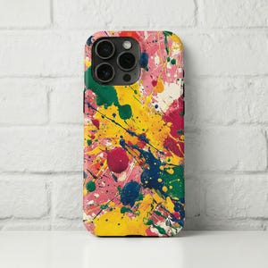 Puede incluir: Una funda de teléfono colorida con un vibrante diseño abstracto de salpicaduras de pintura. La funda presenta una mezcla de colores brillantes, incluyendo rosa, amarillo, verde, azul y rojo, creando un aspecto dinámico y artístico. La funda tiene un acabado brillante.